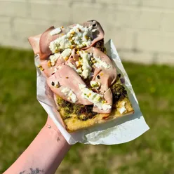 Slice of New York-style pizza with mortadella, mozzarella, pesto, and pistachio from The Bristol Loaf, Bristol, UK.