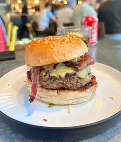 Juicy burger with American cheese, crispy bacon, bacon jam, and pickles at Prime by Pasture, Bristol. Served with fries and salted caramel gelato.