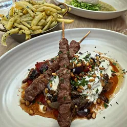 Wood grilled lamb skewers with roast peppers, onion salad, garlic yoghurt, and garlic butter fries at 1 York Place Bristol.