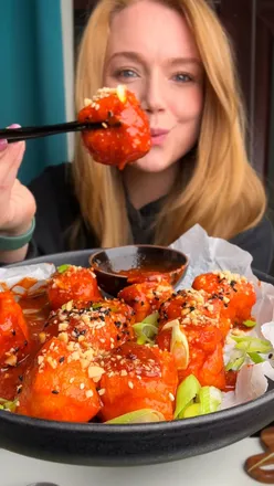 Glossy gochujang-coated tofu puffs topped with spring onions and peanuts, perfect for vegan food lovers.