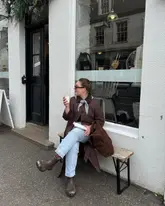 Person wearing a neckerchief and trench coat, enjoying the charming shops and scenery of Dunkeld, Scotland.