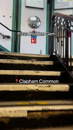 Food reviewer enjoying pizza at a Clapham restaurant, sharing a fun anecdote about the area.