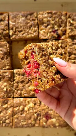 Freshly baked redcurrant and white chocolate crumble blondies, topped with streusel, in a square dish on a wooden surface.