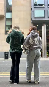 Two friends wearing stylish @blakely_women hoodies, smiling and enjoying each other's company in a vibrant setting.