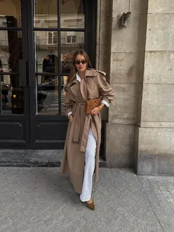 Model wearing a stylish trench coat in a trendy urban setting during fall season.