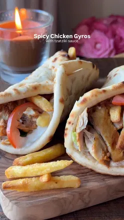 Spicy chicken gyros wrapped in flatbread with tzatziki, tomatoes, lettuce, and fries, perfect for a flavorful lunch.