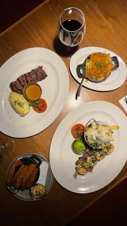 Couple enjoying a delicious steak dinner at The McMillan in Glasgow, featuring sides, sauces, and a bottle of wine.