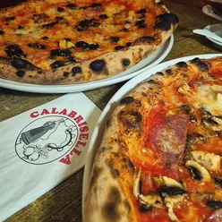 Diners enjoying giant pizzas and delightful starters at Calabrisella Canton, Cardiff, featuring rustic decor and friendly service.