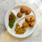 Delicious Bataka Vada and Tuver Kachori served with green chili and chutneys for a satisfying lunch experience.