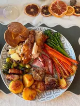 A top-down, well-lit photograph of a traditional British Christmas roast dinner, featuring roast chicken, potatoes, pigs in blankets, stuffing, and vegetables. The image is captured in a home-cooking style with thematic dried orange decorations, presenting a warm and festive atmosphere.