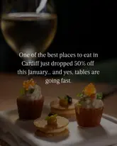 A sophisticated, moody close-up shot of refined canapés or amuse-bouche, likely from a high-end brasserie. The lighting is dramatic and focused, effectively highlighting the textures of the food against a dark, out-of-focus background, which creates an elegant and premium atmosphere.