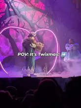 A low-light, audience-perspective shot of a live theatre production of Beauty and the Beast, featuring two actors on stage framed by a large, glowing neon heart prop.