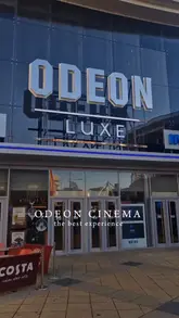 A short vlog-style video showing a couple's visit to an Odeon Luxe cinema, covering the exterior, the self-service ordering kiosks, the food selection, and the entrance to the iSense screen.