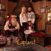 A professional-style event photograph capturing a family meet-and-greet with Santa Claus at a Lapland UK venue, featuring a festive, decorated set.