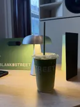 A simple, straightforward shot of an iced matcha latte in a takeaway cup, placed on a table in a cafe setting. The image captures the product clearly but lacks professional styling or lighting to make it stand out as a compelling marketing asset.