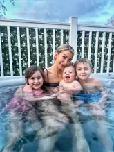 A candid family lifestyle photo featuring a mother and her three children in a hot tub, likely at a holiday lodge. The image captures a happy, relatable moment, effectively promoting the family-friendly nature of the venue.