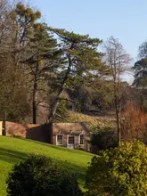 A high-quality, atmospheric landscape photograph of a historic brick garden structure, likely a folly, nestled into a grassy hillside at Newark Park. The image utilizes beautiful golden hour lighting to accentuate the textures of the building and the surrounding landscape, creating a serene and inviting scene.