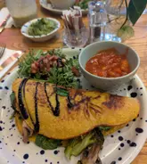 A top-down shot of a vegan omelette served with a side salad and a bowl of beans, captured in a cafe setting.