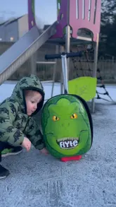 A short video featuring a young child packing a dinosaur-themed scooter suitcase and riding it to a local park. The video highlights the product's functionality as a suitcase, trolley, and scooter.