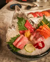 A high-quality, close-up shot of a premium sashimi platter served on a bed of ice, featuring various cuts of raw fish, garnished with shiso leaves and citrus. The lighting is warm and inviting, highlighting the fresh texture of the fish.