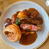 A high-quality, overhead food photography shot of a Sunday roast dinner, featuring a perfectly cooked fillet steak, golden roast potatoes, a Yorkshire pudding, and rich gravy, served on a simple wooden table.