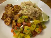 A top-down, functional shot of a home-cooked meal featuring jerk tofu, coconut rice, and pineapple salsa. The image captures the components clearly but lacks the professional lighting and deliberate plating required for high-end hospitality marketing.