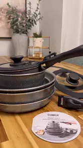 A product demonstration video showcasing a 13-piece non-stick cookware set from Tower. The video uses a top-down, static tabletop perspective to highlight the stackable design, detachable handles, and silicone lids, accompanied by text overlays explaining the features.