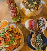 A top-down flat lay shot of a spread of bao buns and loaded fries served on a wooden board. The image captures a variety of dishes including different types of bao buns and loaded fries, presented in bamboo steamers and on a wooden surface.
