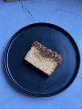 A top-down, overhead shot of a single slice of cake served on a black plate against a blue-toned surface. The image suffers from a significant, unnatural cool colour cast that detracts from the visual appeal of the food.