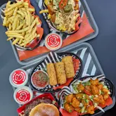 A high-angle, flat-lay photograph showcasing a variety of fast-food items from Big Licks, including a smash burger, loaded fries, mozzarella sticks, and a side of pancakes. The image is well-lit and clearly composed, effectively displaying the menu items in branded packaging on a neutral surface.