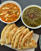 A high-quality, overhead shot of a South Indian and Sri Lankan meal featuring two bowls of curry and a stack of parotta bread arranged on a dark, minimalist surface.