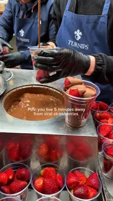 A short, high-quality clip capturing the preparation of chocolate-covered strawberries at a market stall in Borough Market, London. The video focuses on the dipping process, highlighting the fresh fruit and rich chocolate coating.