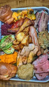 A fast-paced, engaging review of a BBQ-style Sunday carvery in Manchester. The video features a large sharing tray of smoked meats, including brisket, turkey, and pork belly, alongside various sides like broccoli cheese and Yorkshire puddings. The creators demonstrate the food's quality through close-ups and taste tests, highlighting the unique fusion of traditional Sunday roast and BBQ techniques.