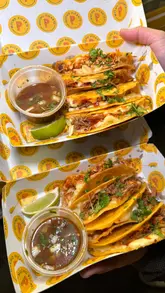 A short, high-energy promotional video for Mucho Picante, a street food vendor specializing in birria tacos. The video features quick cuts of the food truck, close-ups of the tacos being dipped in consommé, and a display of the menu and drink options.
