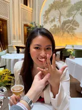 A high-quality, well-composed lifestyle shot capturing an engagement celebration at a luxury hotel. The focus is sharp on the ring, with the subject's expression conveying joy, set against an elegant, well-lit background.