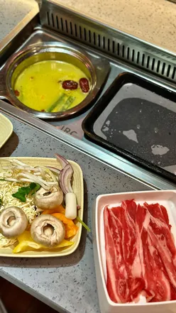 Guests enjoying a unique BBQ and hotpot dining experience at DAIU in Cardiff Bay, surrounded by various meats and vegetables.