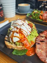 A close-up, appetizing shot of a brunch dish featuring poached eggs on avocado toast with a side of bacon, captured in a casual cafe setting.