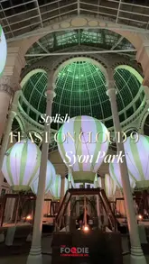 A montage video showcasing the 'Feast on Cloud 9' dining experience at Syon Park's Great Conservatory. The video highlights the unique hot air balloon-themed dining pods, the elegant conservatory setting, and various courses of the meal, including starters, mains, and desserts.