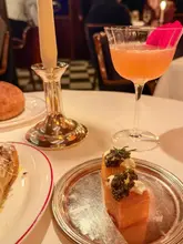 A high-quality, atmospheric shot of a table setting at a fine dining restaurant, featuring crispy potato cakes topped with caviar and a cocktail. The image effectively captures the mood and elegance of the venue.