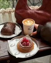 A high-quality, aesthetically pleasing shot of a bakery table featuring a latte and two pastries. The image uses natural light and a shallow depth of field to create an inviting, cozy atmosphere, typical of a lifestyle-focused cafe review.