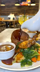 The creator visits Nova Scotia in Liverpool to review their Sunday roast offering. The video features a walkthrough of the venue, highlighting the cozy interior and the view, followed by a detailed look at the roast chicken and nut roast dishes, including a gravy pour and a dessert finish.