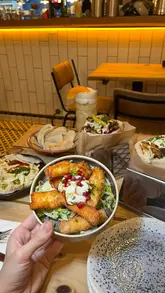 A montage video showcasing various dishes and drinks at Zhug in Nottingham, including hummus, pita, wraps, and desserts, set to music with text overlays.