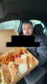 A review of a 'munchie box' and a club sandwich from Katie's Kitchen, filmed by two creators in a car. The video focuses on the quality and portion size of the takeaway food.