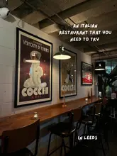 A static interior shot of an Italian restaurant in Leeds, featuring a bar seating area with vintage-style posters on the wall.