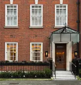 A professional, eye-level architectural photograph of the exterior of Bonheur restaurant in Mayfair. The image captures the classic red brick facade, symmetrical windows, and the elegant glass canopy entrance, conveying a sense of prestige and high-end hospitality.