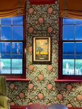 A perfectly symmetrical, high-quality interior shot of a hotel room or lounge at Beaverbrook Townhouse. The image features distinctive pineapple-patterned wallpaper and a framed vintage-style print of 'The Zoo' positioned centrally between two windows, showcasing the venue's sophisticated and curated aesthetic.