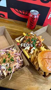 A food review video featuring a creator eating a fried chicken burger, loaded fries, and coleslaw from Fed's Fried Chicken, providing reactions to the food.