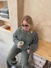 Fashionable woman holding a matcha latte in a bright London coffee shop.