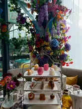 A photograph of a three-tiered afternoon tea stand set against a vibrant, floral-decorated window backdrop at a restaurant in Borough Market.