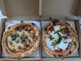 A top-down shot of two pizzas in cardboard takeaway boxes, showcasing a Mortadella pizza and a Partenope pizza.